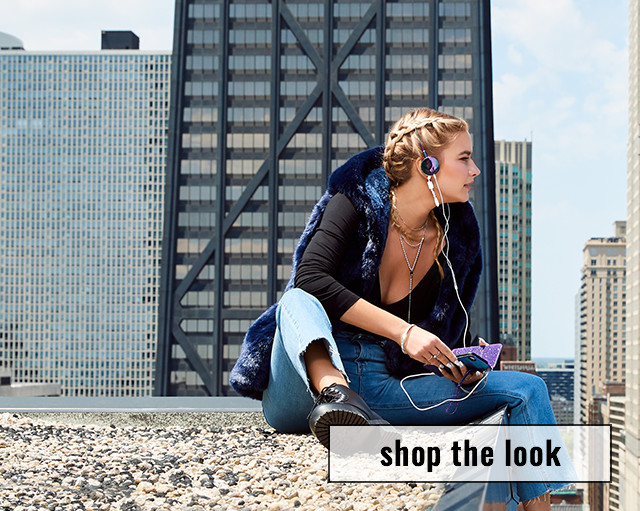 woman looking over rooftop with fur vest and headphones